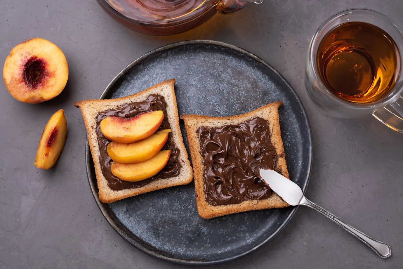 plate-toast-with-chocolate-paste-with-peach-slices-plate-with-cup-tea-gray-concrete-background.jpg